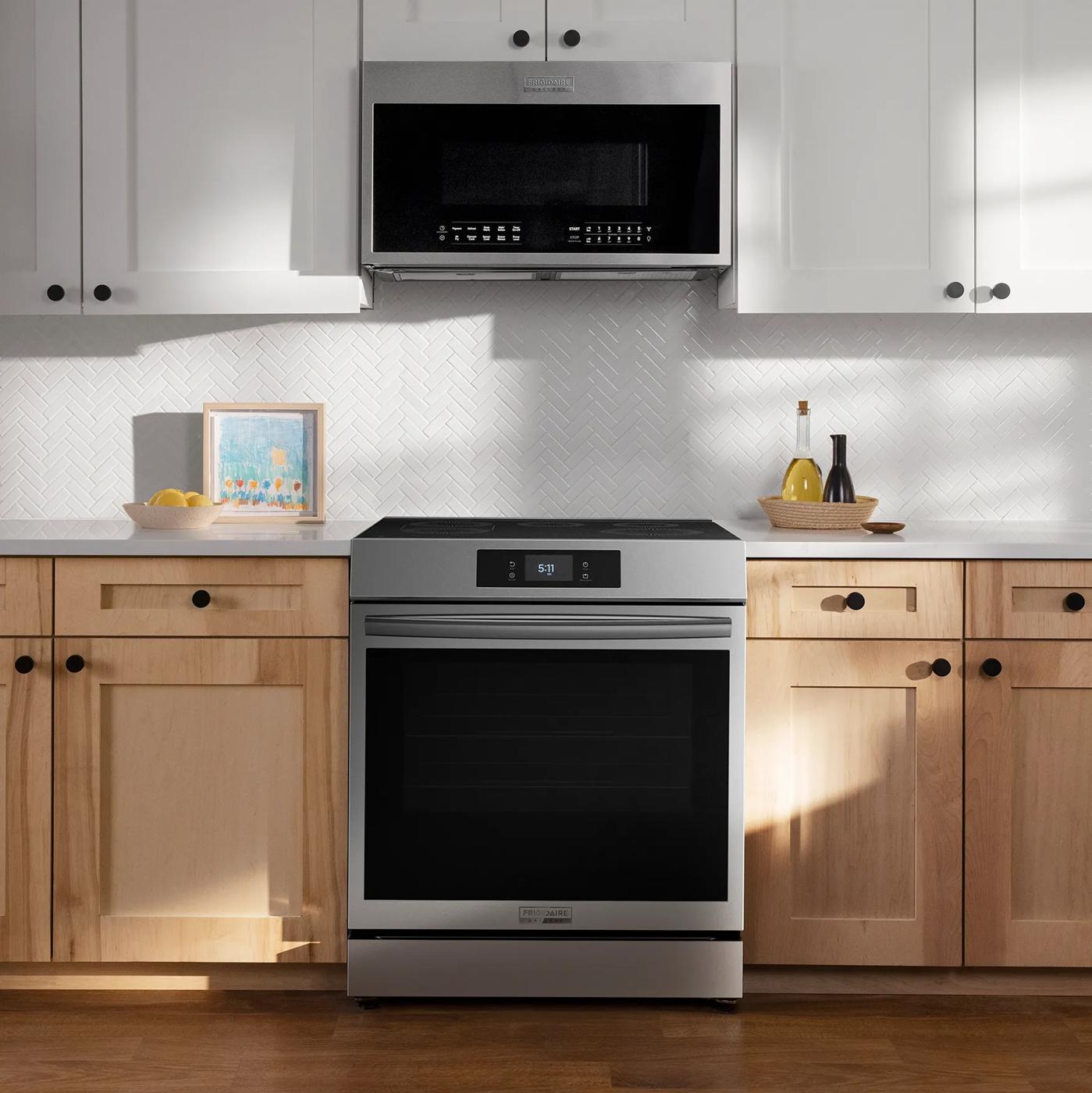 Stainless steel front control induction range with digital display installed between light wood cabinets in a modern kitchen