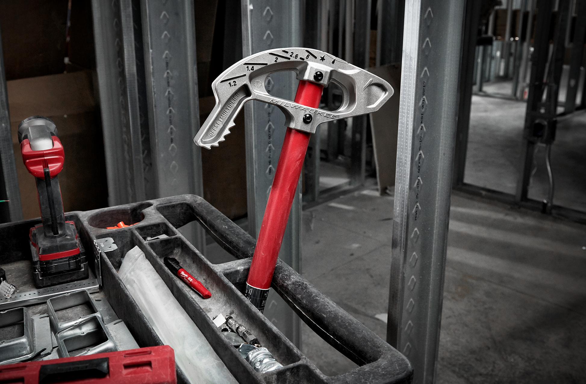 Red-handled aluminum conduit bender with angle markings resting in a tool cart at a construction site