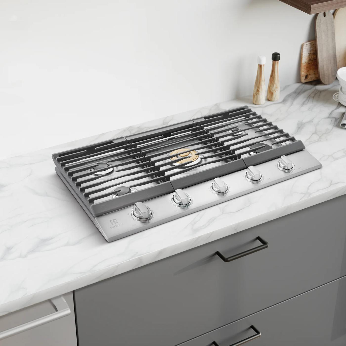 Stainless steel 36-inch gas cooktop with five burners and front control knobs in modern kitchen setting for home improvement