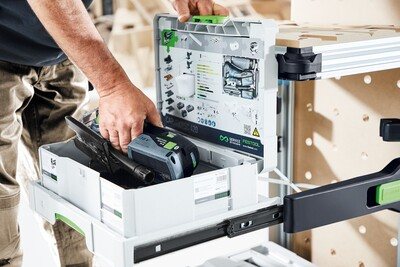 Hand placing black and gray cordless tool battery into white and green pull-out drawer for workshop storage organization system