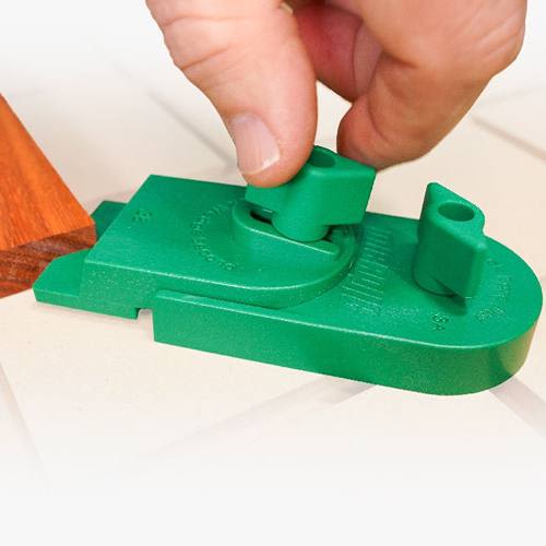 Hand adjusting green plastic ramp clamp tool on white surface for precise woodworking and home improvement tasks