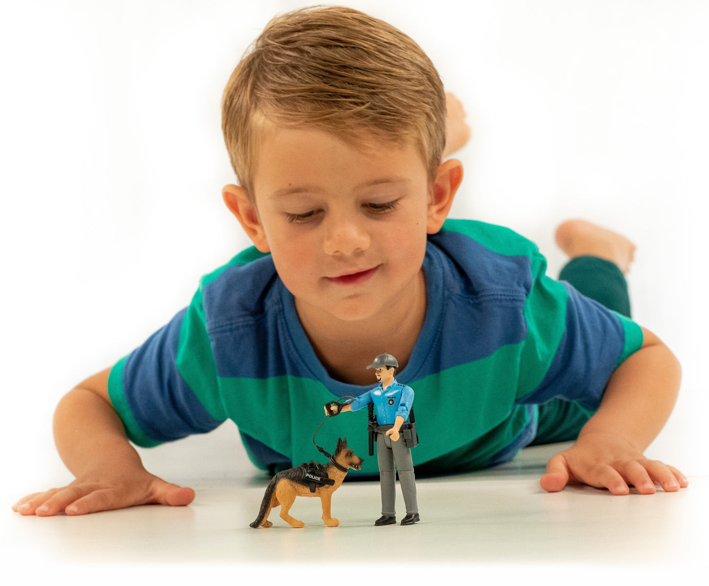 Young boy lying on floor playing with a police officer figure and a German Shepherd dog toy in harness