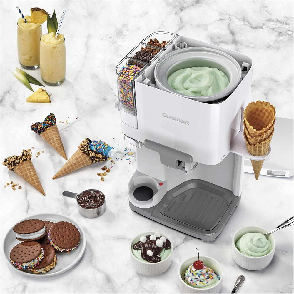 Compact white soft serve ice cream maker with mix-in dispenser, waffle cones, and various ice cream treats on marble surface