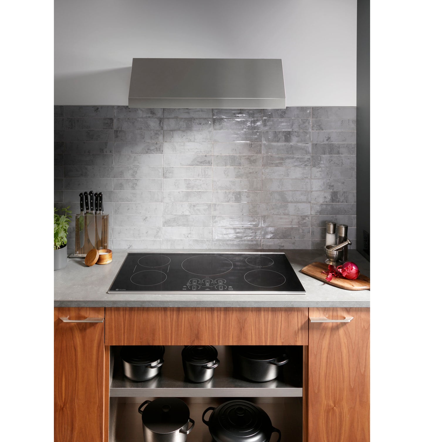 Built-in black glass induction cooktop with touch controls installed in a kitchen with wood cabinets and stainless steel vent hood