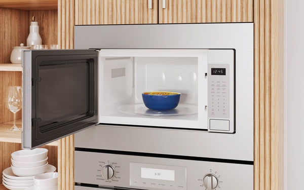 Built-in stainless steel microwave with left side door open, showing interior bowl and digital control panel in kitchen setting