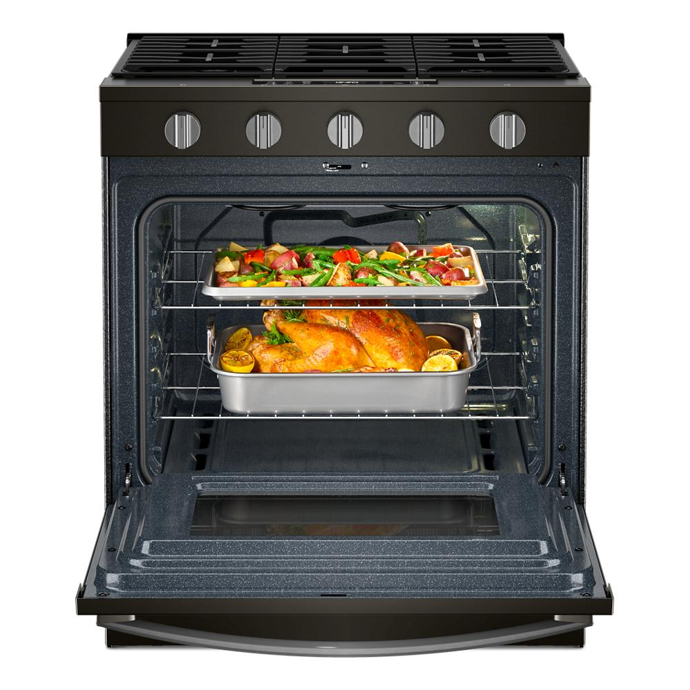 Open 30-inch gas range oven with two trays of roasted chicken and vegetables inside, shown in kitchen appliance setting