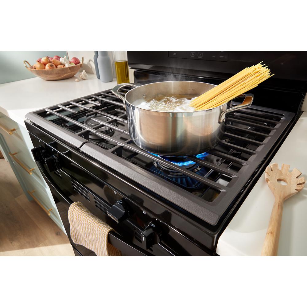 Black gas range with stainless steel pot boiling water and spaghetti on front burner in kitchen setting