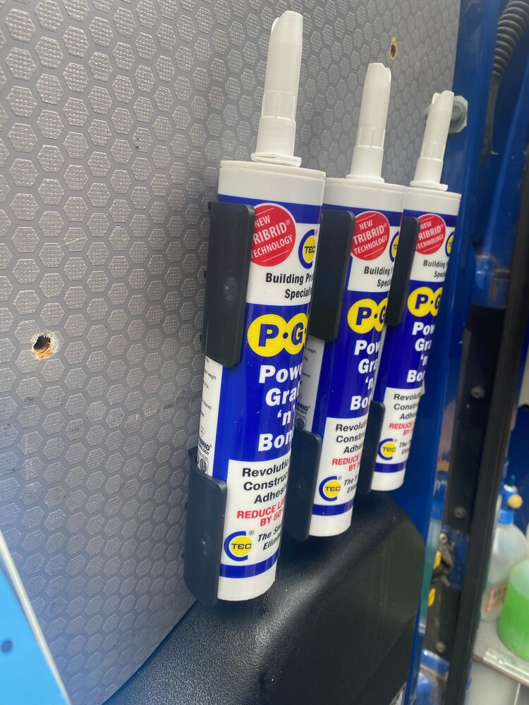 Black mounts holding blue adhesive tubes on a textured wall, ideal for garage storage and home improvement tools organization