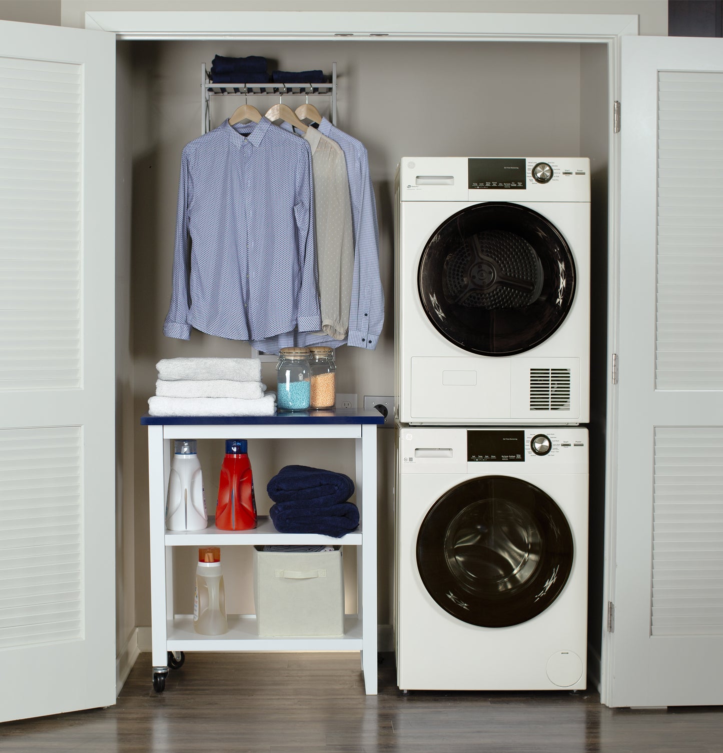 Compact laundry closet with stacked white front load washer and dryer, organized shelving, and hanging shirts in front load washers collection
