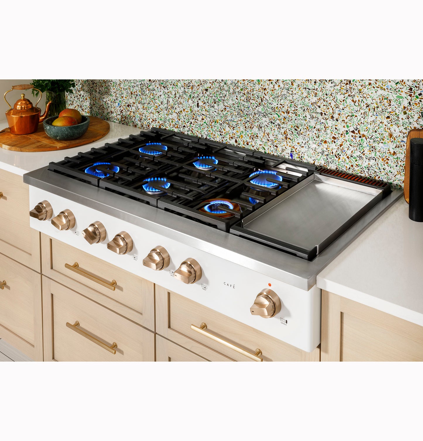 Modern kitchen cooktop with six active gas burners and integrated griddle in a stylish light wood cabinetry setting