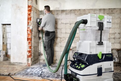 Festool diamond grinder connected to dust extractor in unfinished room during home improvement work