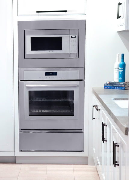Built-in stainless steel microwave with left side opening door above a built-in stainless steel oven in modern kitchen