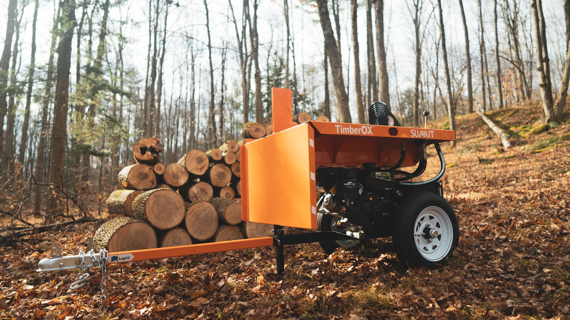 Orange log splitter with black engine and white wheels positioned near stacked logs in forest for home improvement use