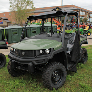 Green John Deere Custom XUV835M utility vehicle with full roof and rugged tires parked on grass outside a building