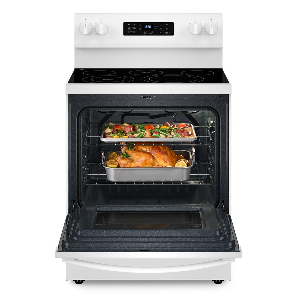 Open white electric range oven with roasted chicken and vegetables baking on two racks in kitchen appliance setting