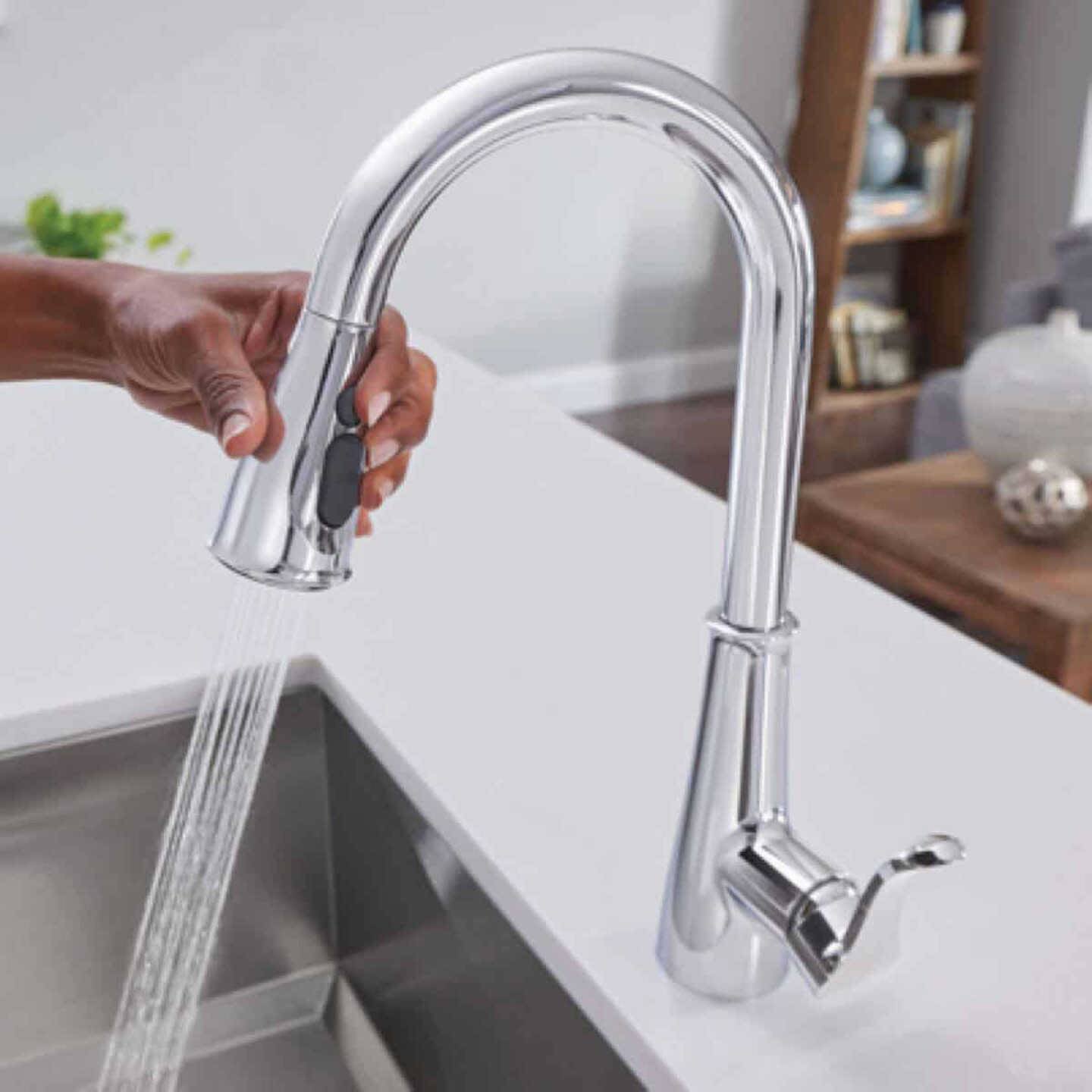 Hand operating chrome high arc pulldown kitchen faucet dispensing water into stainless steel sink for home improvement