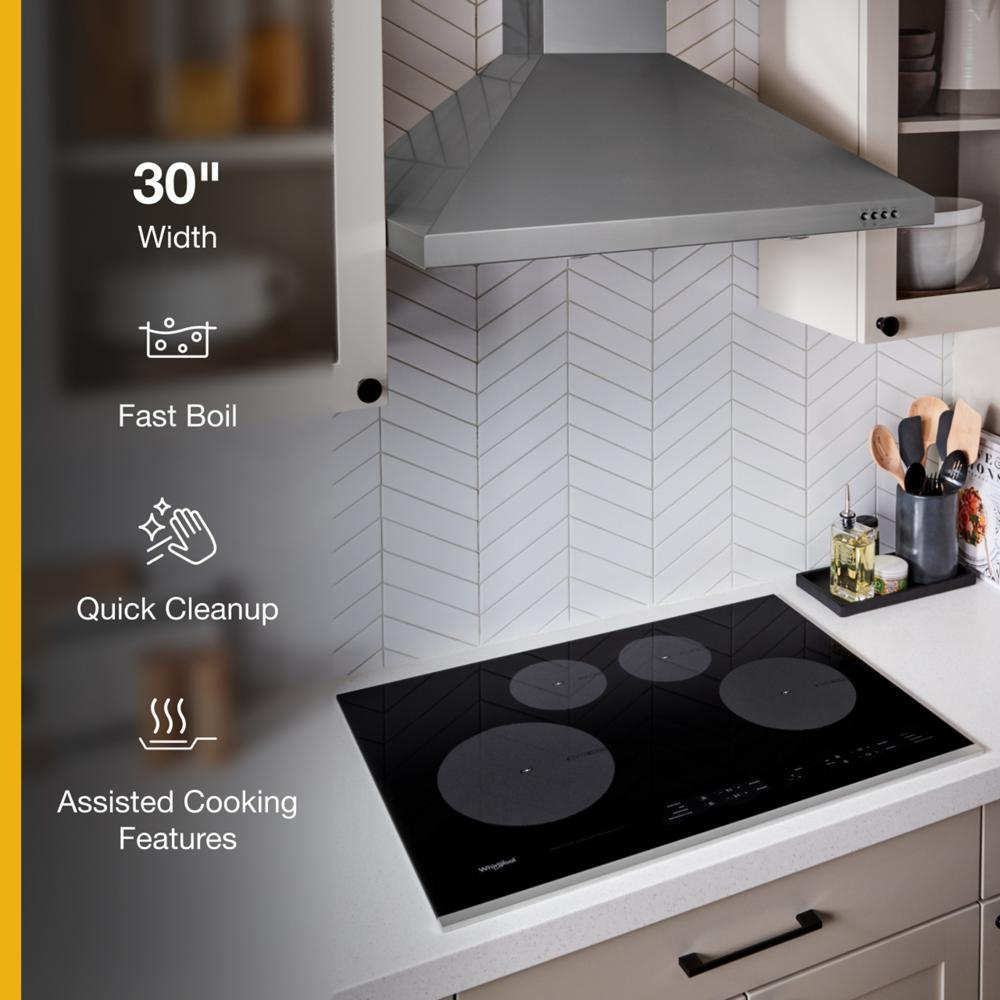 Sleek black glass induction cooktop with four cooking zones installed in modern kitchen countertop with stainless steel range hood above