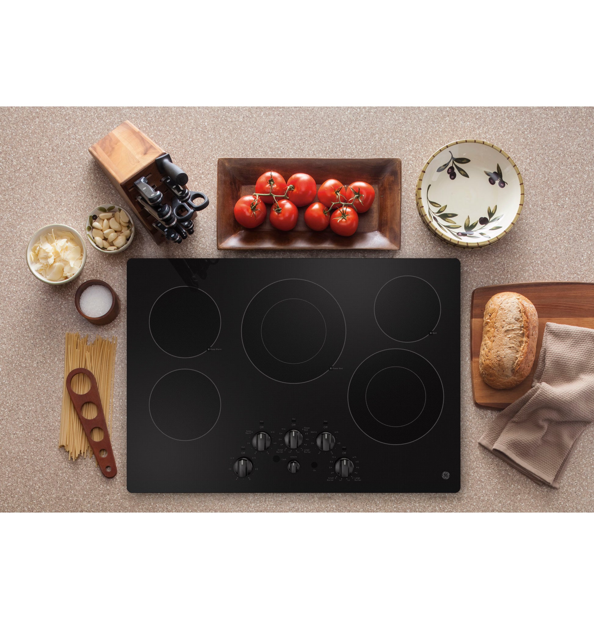 Black built-in electric cooktop with five burners and knob controls, styled with cooking ingredients on a kitchen countertop