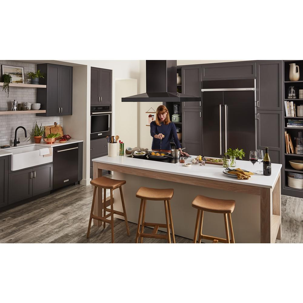Contemporary kitchen with dark gray cabinetry, white island, and a cooktop where a woman prepares food with wine glasses nearby