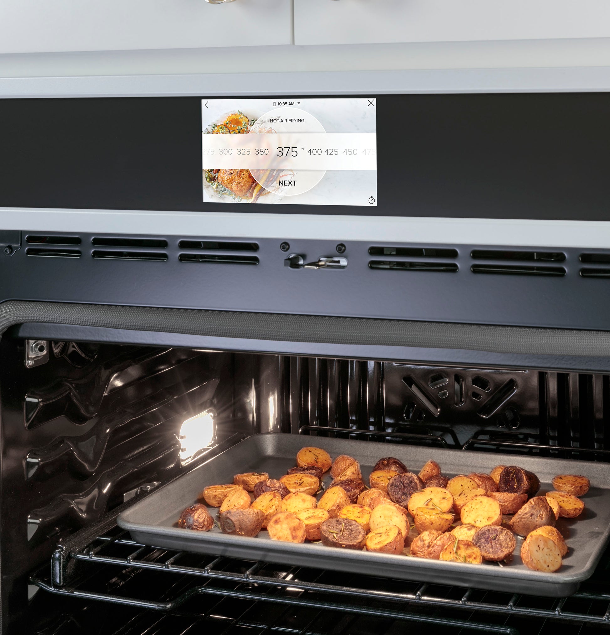 Smart built-in convection oven with digital touchscreen and a baking tray of seasoned potatoes inside appliance