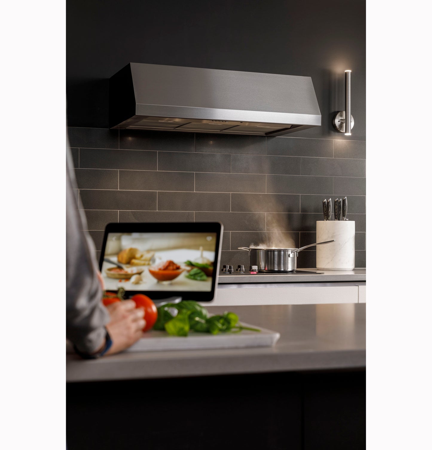 Industrial stainless steel range hood mounted above stovetop with cooking pot and kitchen tools nearby in modern kitchen