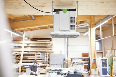 White and green ceiling mounting bracket suspending an air purifier in a woodworking tools and dust collection workshop