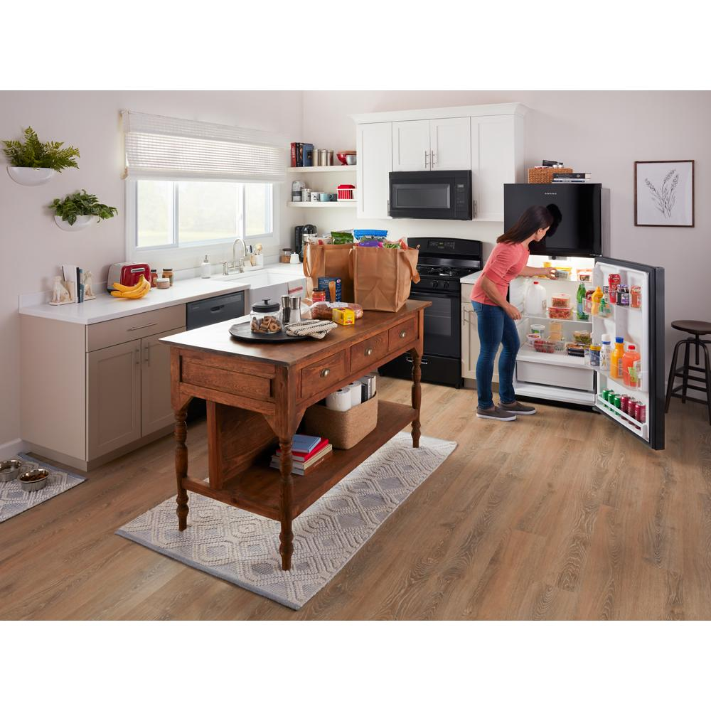 Woman unloading groceries into black stainless steel refrigerator in bright kitchen with wooden island and microwave