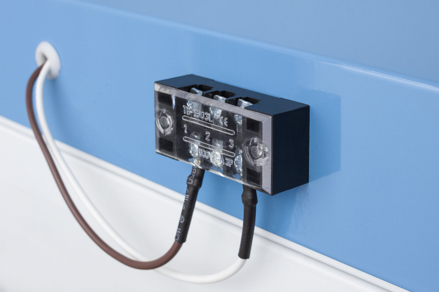 Close-up of electrical terminal block with two wires connected against light blue appliance surface in kitchen appliance setting