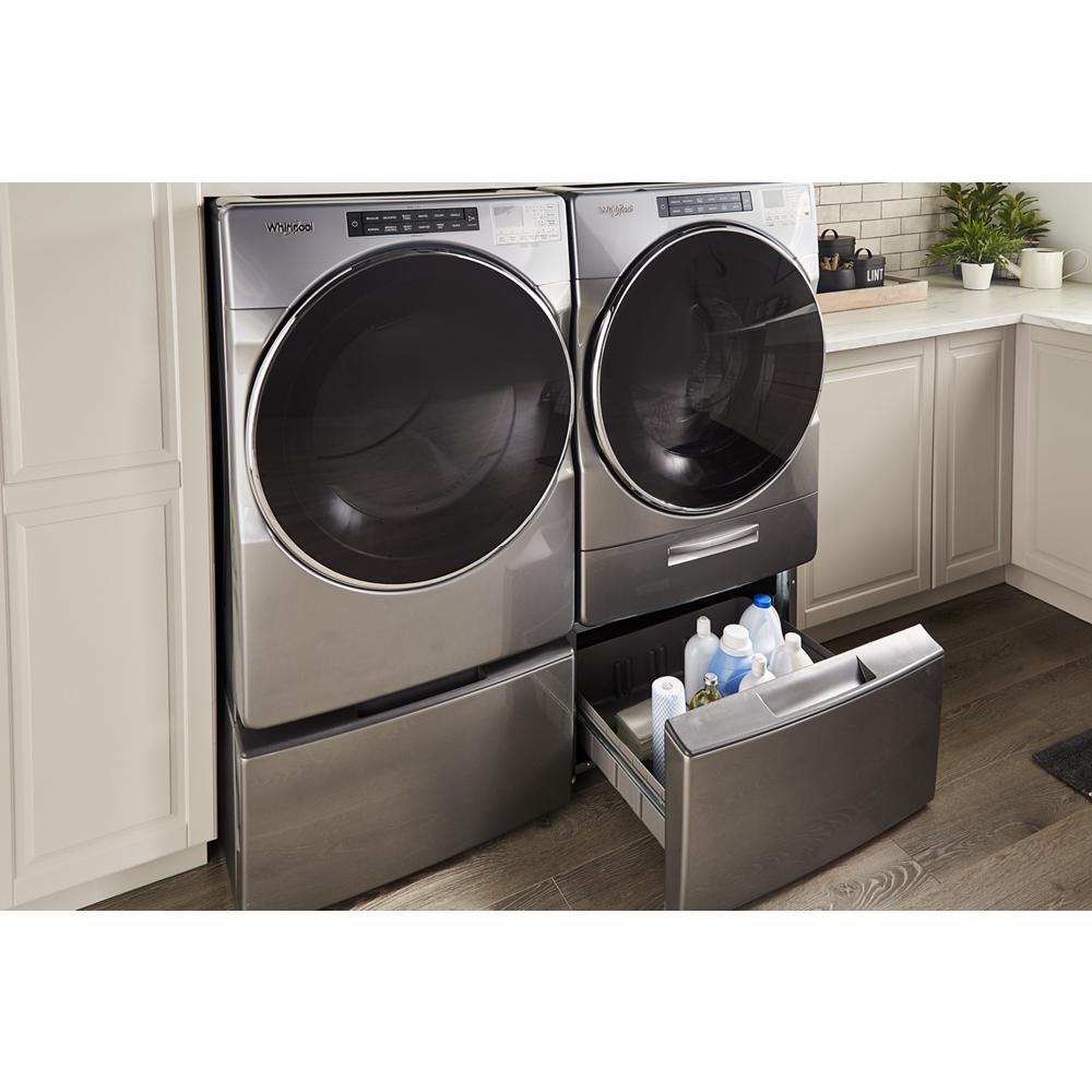 Silver front load washer and dryer on matching pedestals with open storage drawer holding laundry supplies in appliances collection