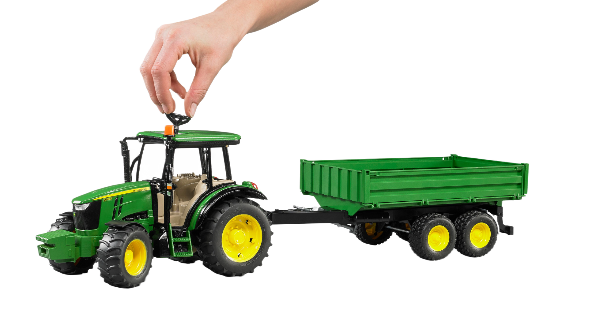 Hand positioning an orange beacon on a green toy tractor model with yellow wheels and matching green trailer