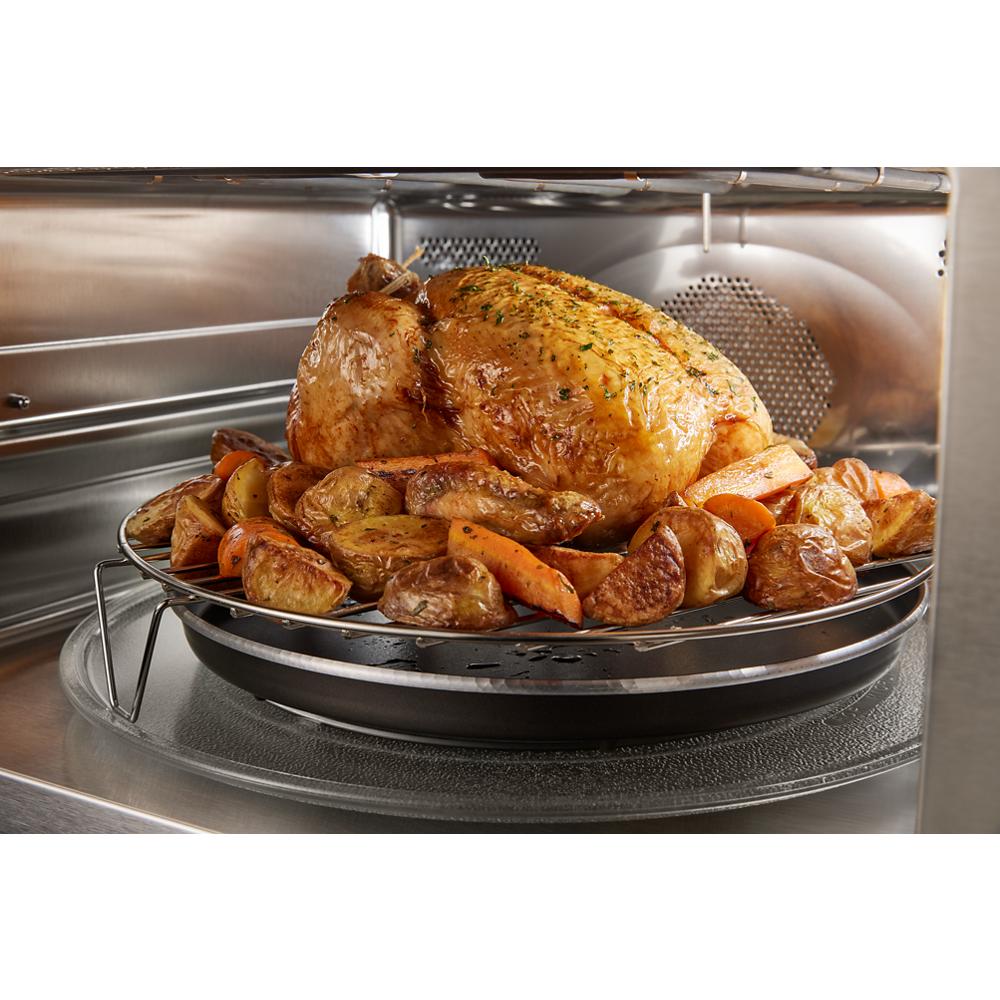 Whole roasted chicken with potatoes and carrots inside stainless steel microwave oven cavity