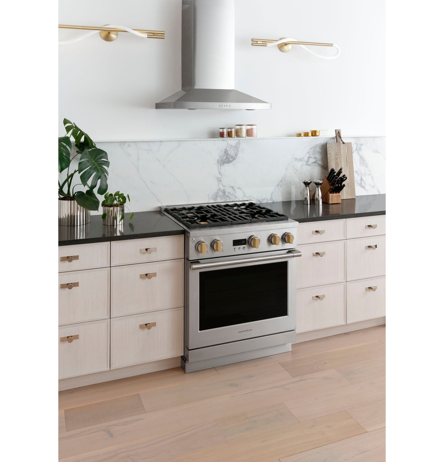 Stainless steel wall-mounted vent hood above gas range with marble backsplash in modern kitchen setting
