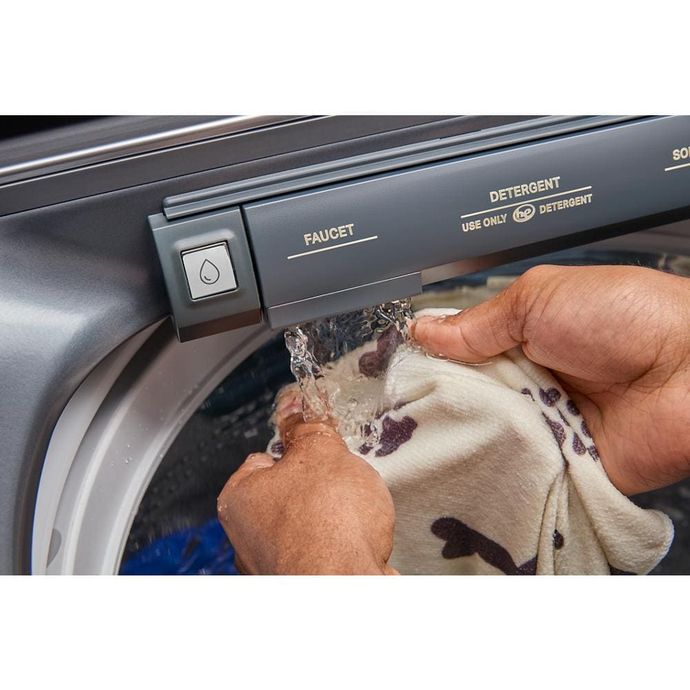 Close-up of hands rinsing pet blanket under faucet on a stainless steel top load washer in home appliance setting