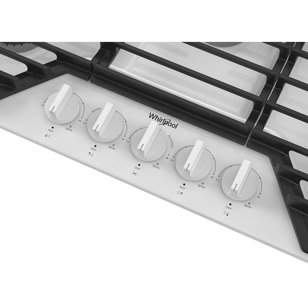 Close-up of five white control knobs on a stainless steel gas cooktop with hinged cast-iron grates for home improvement kitchens