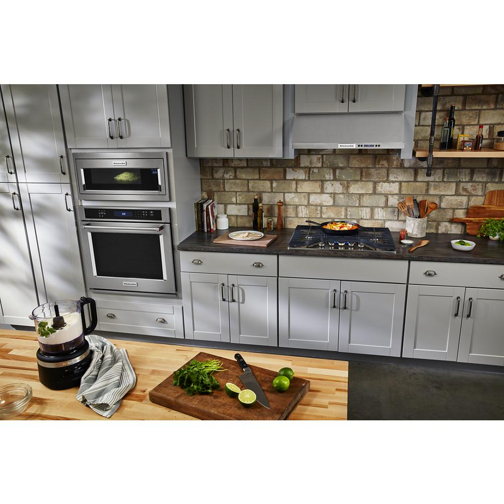 Contemporary kitchen with gray cabinetry, brick backsplash, built-in ovens, under-cabinet ventilation, and wooden prep counter