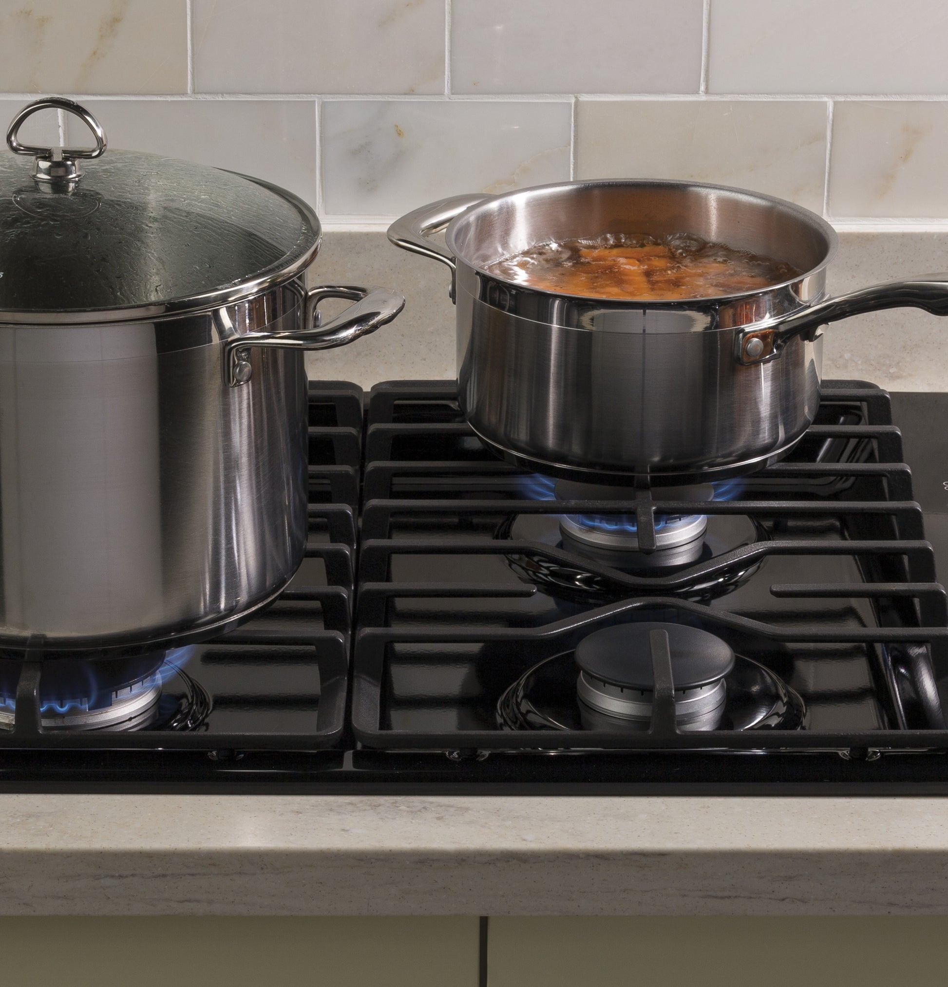 Close-up of two stainless steel pots simmering on a built-in gas cooktop with dishwasher-safe grates in kitchen setting