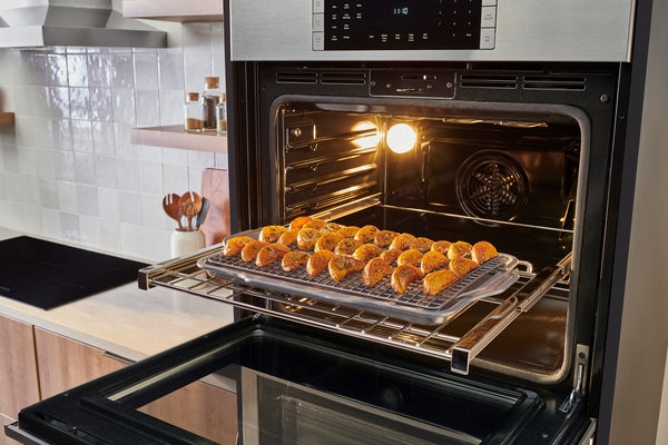 Stainless steel built-in double wall oven with digital display and fresh baked pastries on wire rack inside