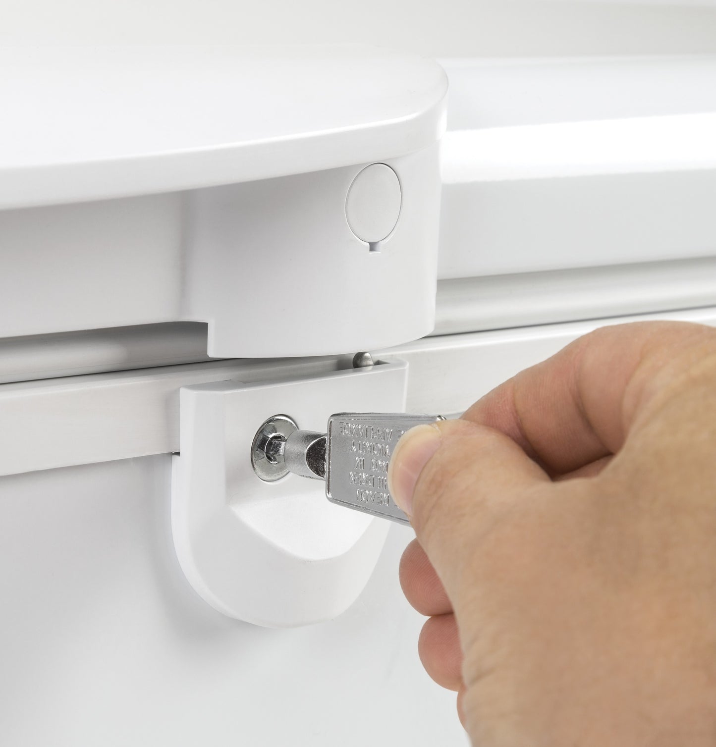 Hand inserting key into lock on white manual defrost chest freezer in kitchen appliance and home improvement setting
