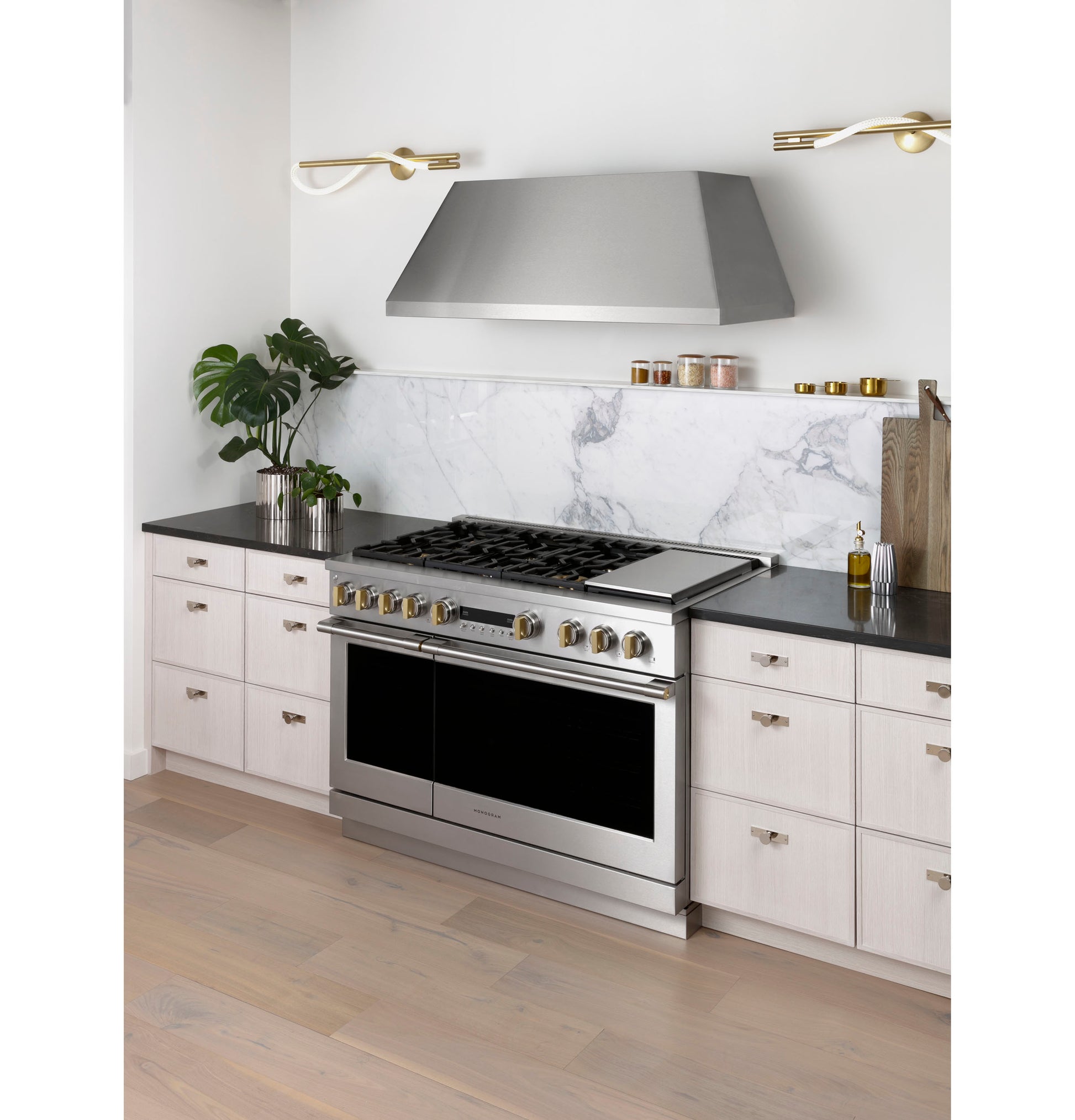 Stainless steel professional kitchen hood installed above range in modern kitchen with light cabinetry and marble backsplash