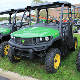 Green John Deere utility vehicle with rugged off-road tires parked on grass in commercial equipment lot