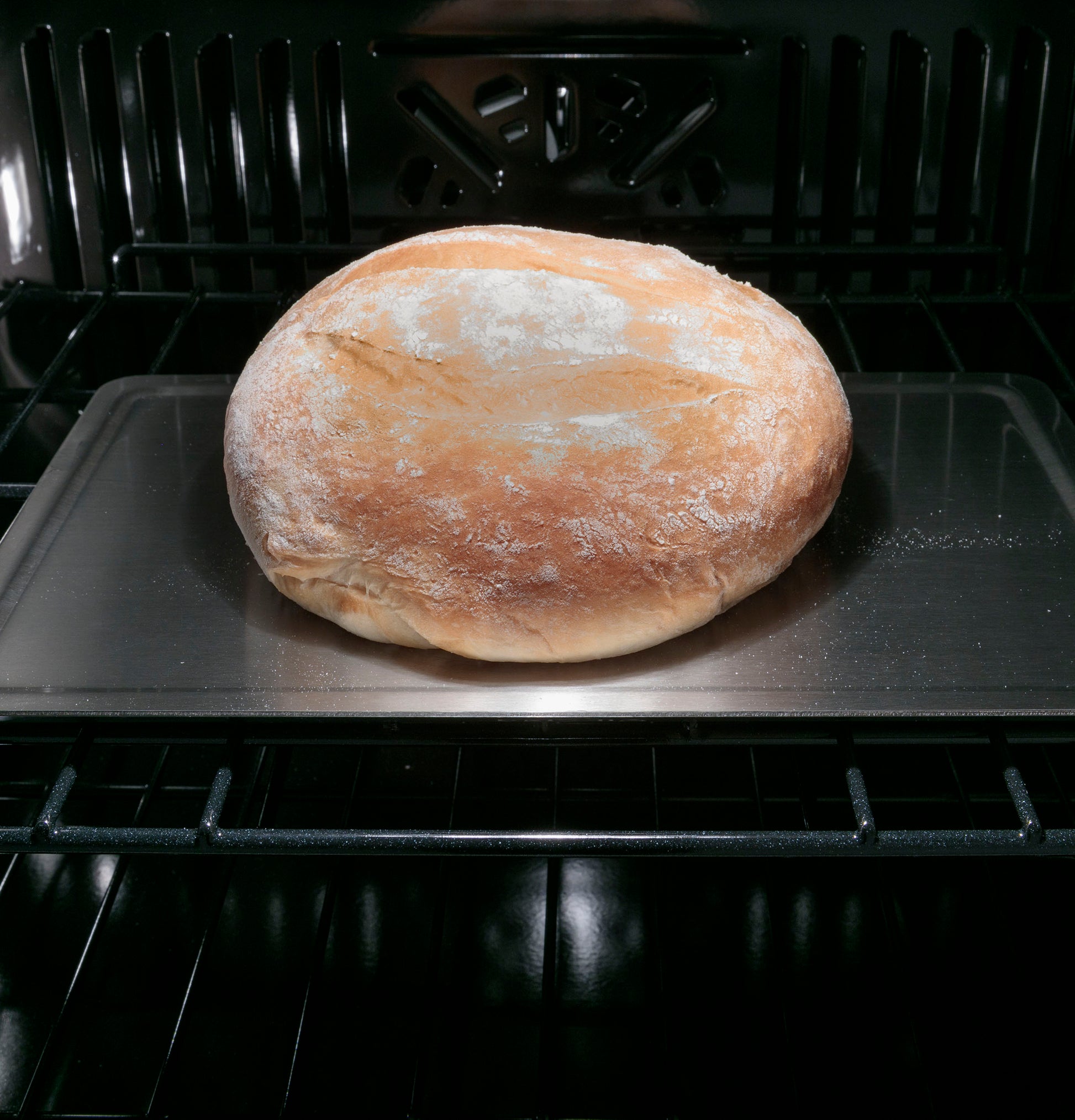 Loaf of bread baking on metal tray inside smart convection single wall oven from kitchen appliances collection