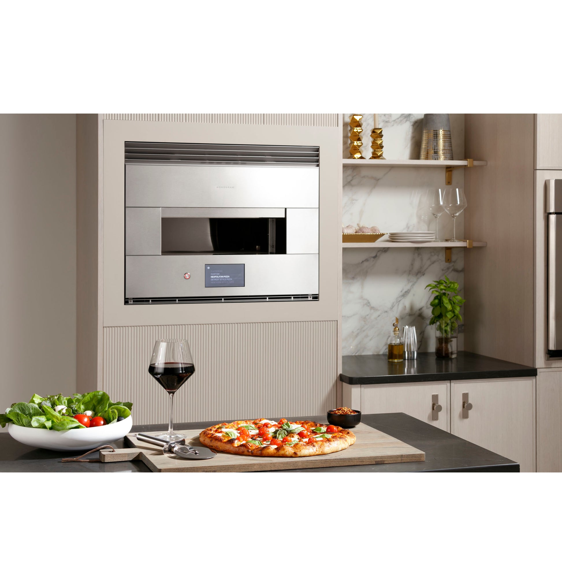 Built-in stainless steel oven with digital display in modern kitchen, pizza on counter with salad and wine glass nearby