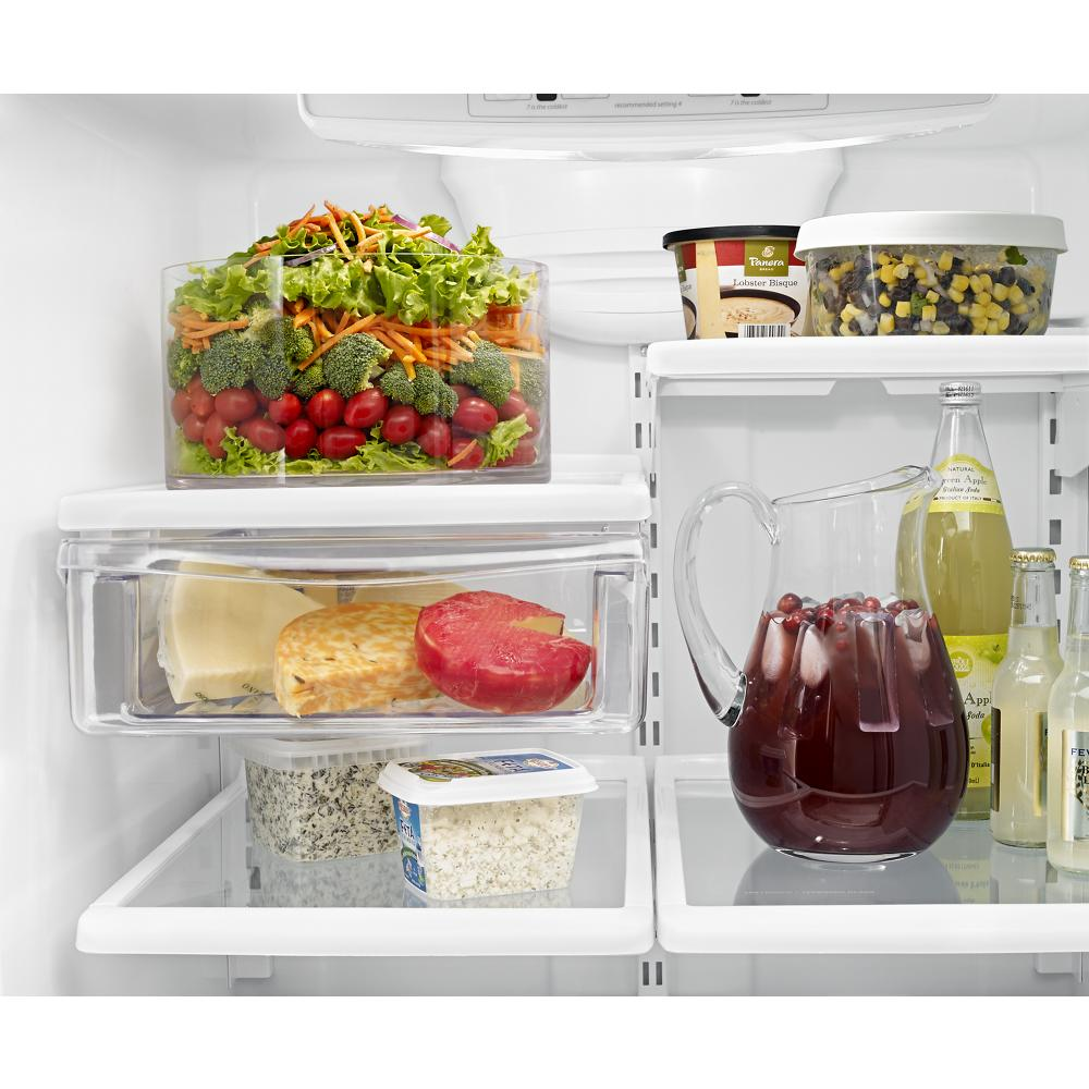 Inside view of bottom-freezer refrigerator showing organized fresh salad, cheeses, beverages, and assorted food containers