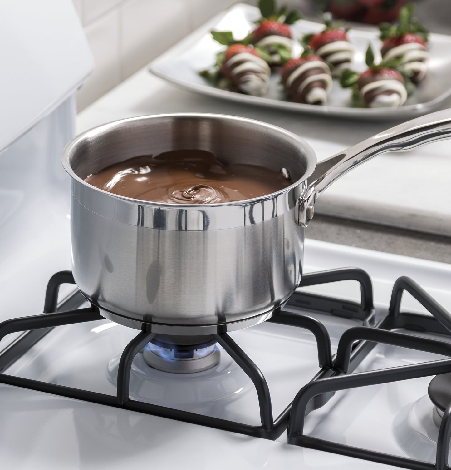 Stainless steel saucepan melting chocolate on white gas burner grate of freestanding range in kitchen setting