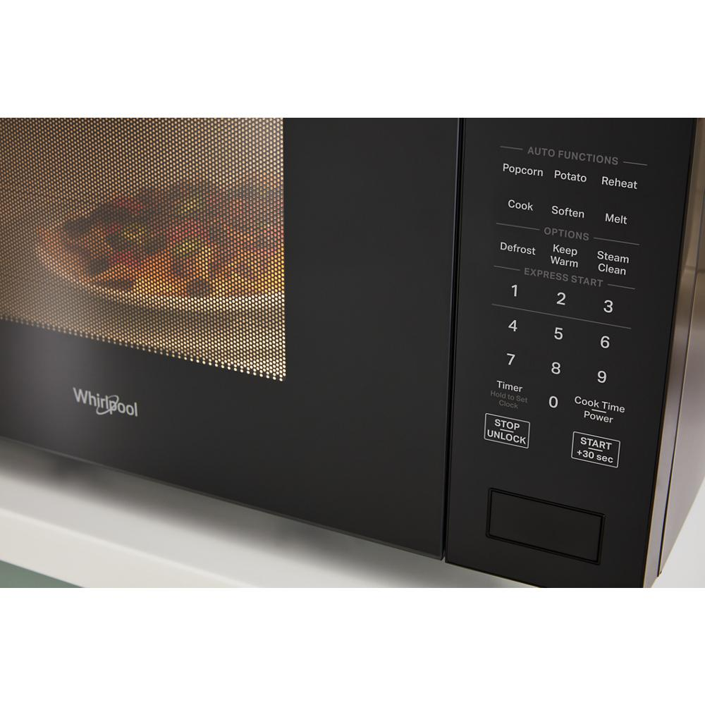 Close-up of black Whirlpool microwave sensor control panel with digital buttons and food cooking inside on white countertop