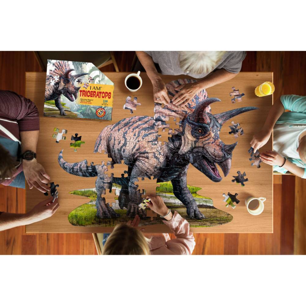 People assembling a 100-piece triceratops puzzle on a wooden table with drinks nearby