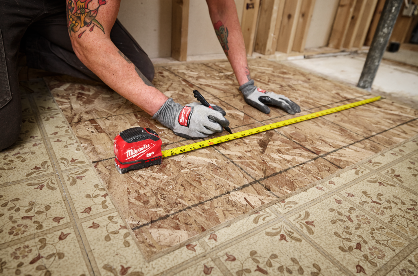 Worker using a 16-foot compact auto-lock measuring tape on plywood for woodworking and home improvement tools