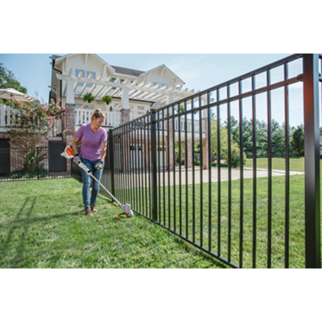Person trimming grass along black metal fence using cordless STIHL battery-powered grass trimmer tool