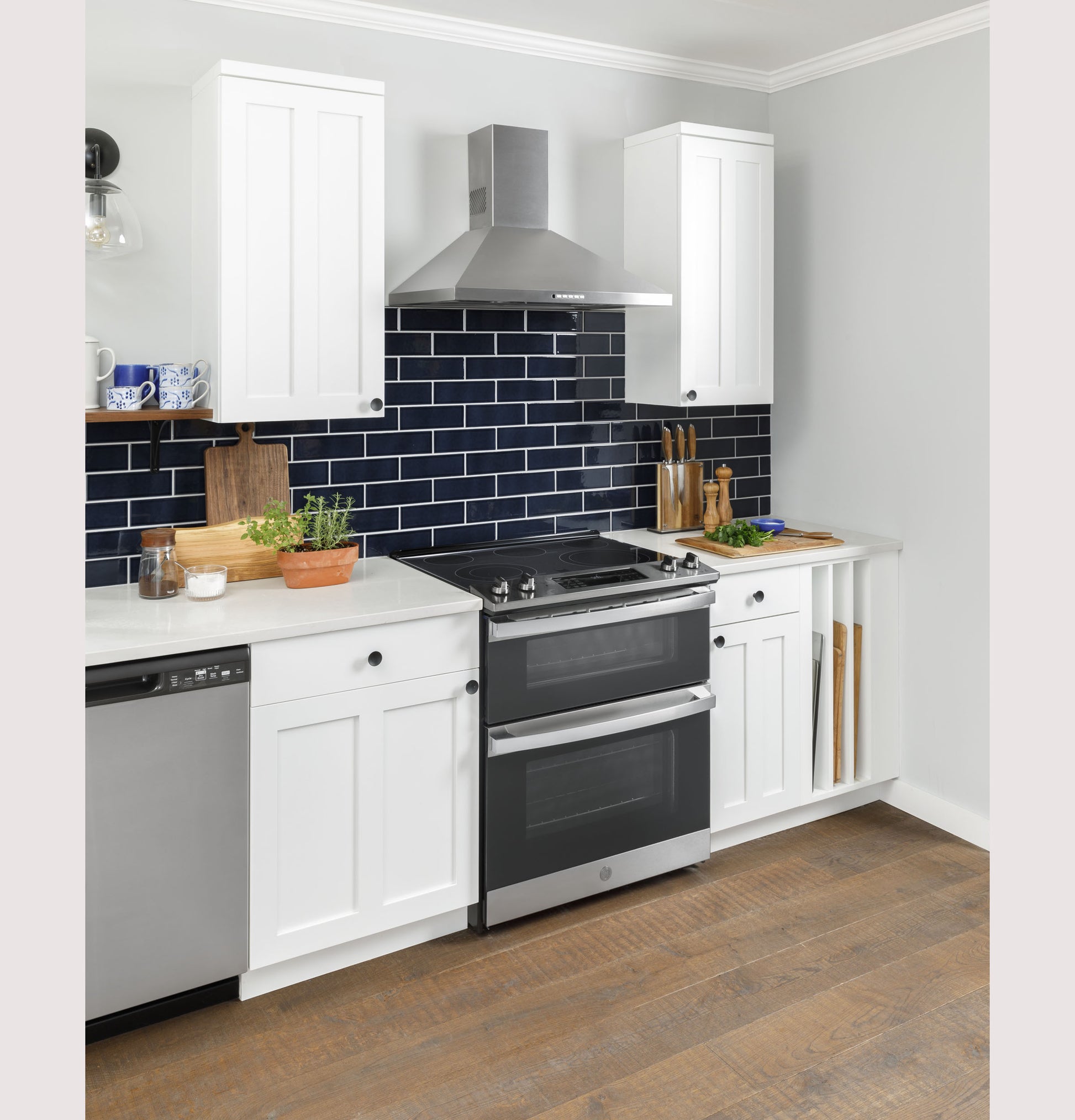 Stainless steel double oven range with electric cooktop in modern kitchen featuring white cabinets and navy tile backsplash