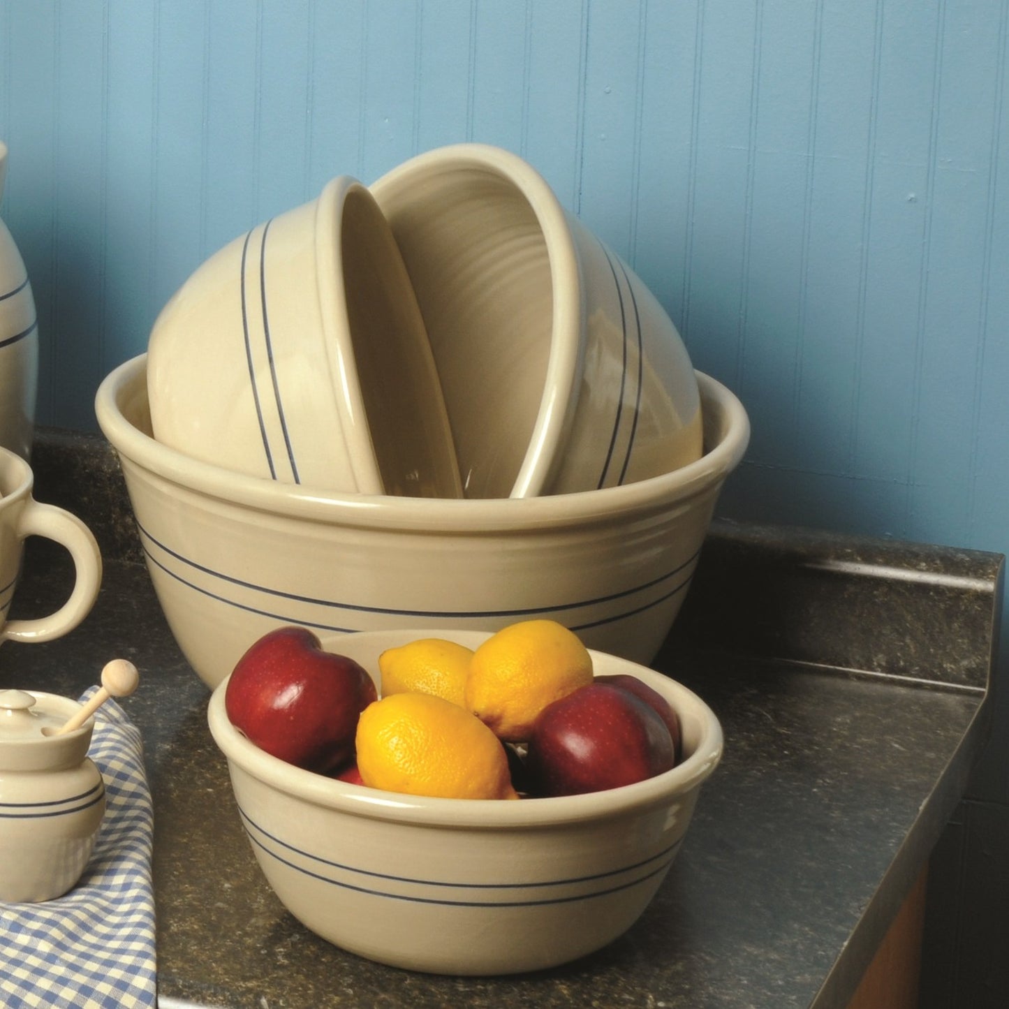 Cream-colored stoneware bowls with heritage blue stripes stacked on countertop with fruit in kitchenware collection